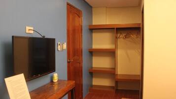 Una habitación con televisión sobre un soporte de madera, una puerta, un perchero y una mesita con un cartel.