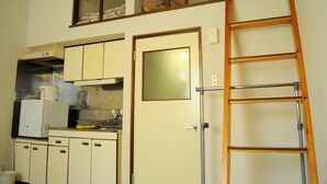 A compact kitchen with a built-in oven, a microwave, and a refrigerator. There is a wooden ladder leaning against the wall and a door with a frosted glass panel. - Petit Hotel Koizumi (Toyako)