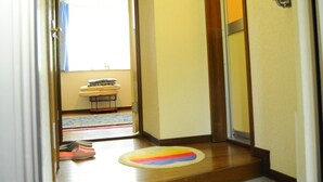A hallway with a wooden floor, a small rug, and a door leading to a room with a bed and a window with curtains. - Petit Hotel Koizumi (Toyako)