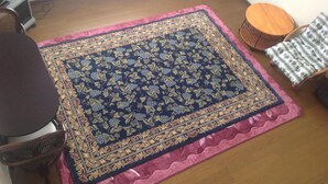 A room with a large patterned rug, a round wooden table, a chair, and a small round table with a patterned cloth. - Petit Hotel Koizumi (Toyako)