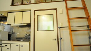 A compact kitchen with a built-in stove, a refrigerator, and upper cabinets. A wooden ladder is positioned against the wall. - Petit Hotel Koizumi (Toyako)
