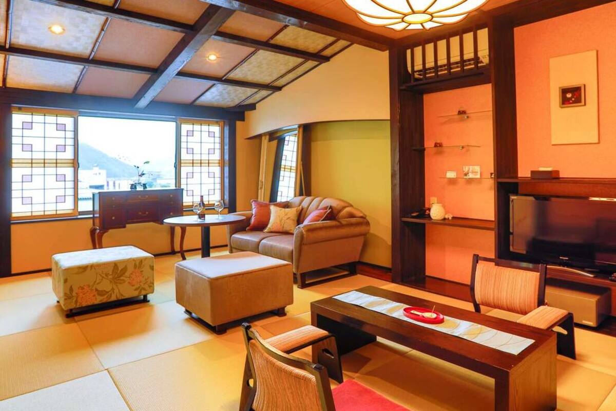 A traditional Japanese-style living room with tatami flooring, a low table, a sofa, and a television.