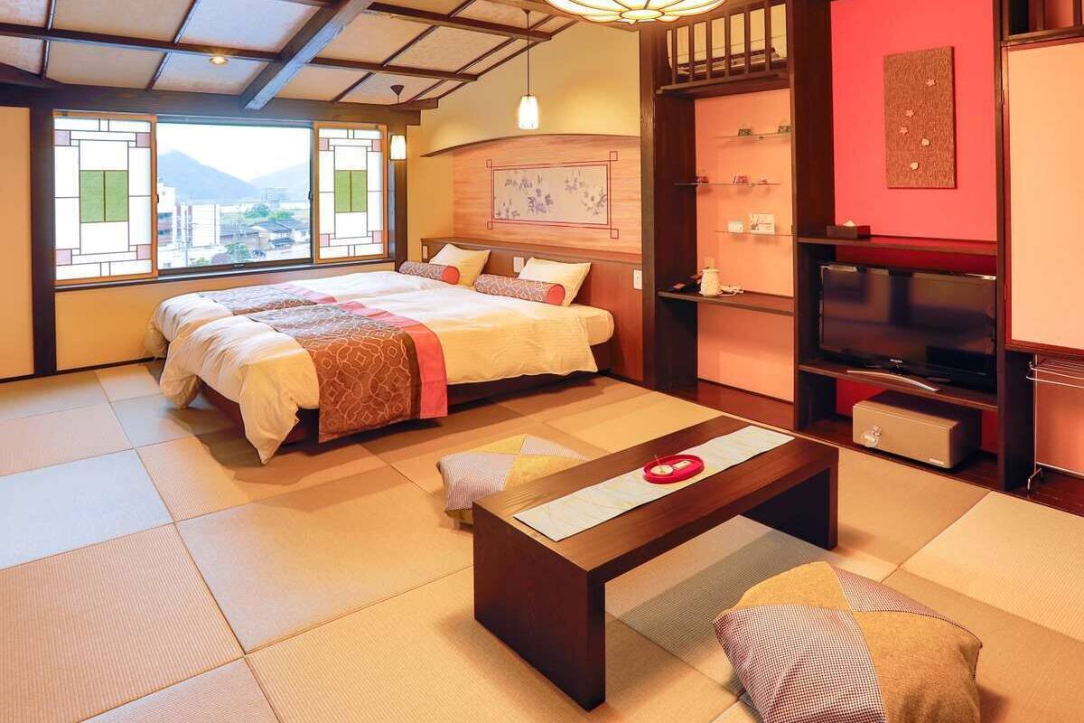 A traditional Japanese-style bedroom with tatami flooring, a bed with a red and white bedding, a wooden coffee table, and a television on a stand.