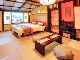 Un dormitorio tradicional japonés con suelo de tatami, una cama con ropa de cama roja y blanca, una mesa de centro de madera y un televisor sobre un mueble.