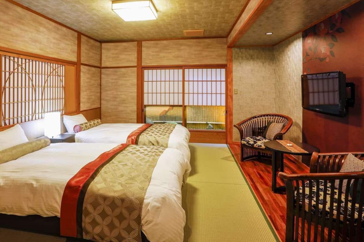 A traditional Japanese-style room with tatami flooring, a futon bed, a low table, and a TV mounted on the wall.