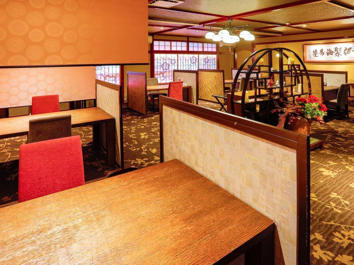 A restaurant with wooden tables and red chairs, partitioned booths, and a decorative vase with flowers.
