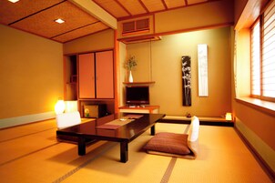 A traditional Japanese-style room with tatami flooring, a low table, a television, and a sliding door.