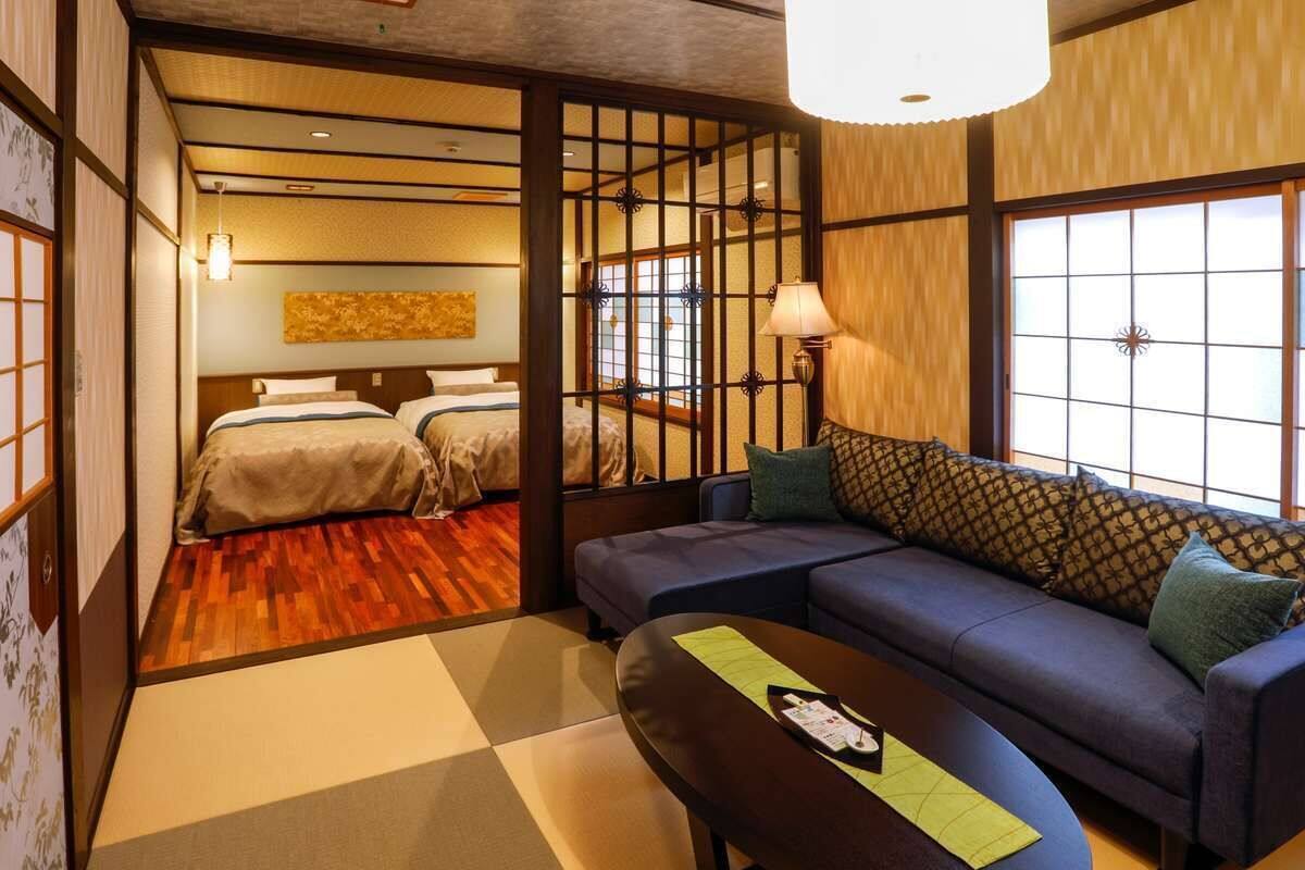 A traditional Japanese-style room with tatami flooring, a low table, a sofa, and a bed with a shoji screen divider.