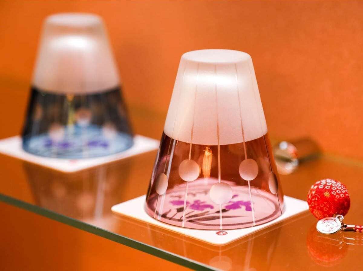 Dos objetos cónicos transparentes con una parte superior blanca, sobre una superficie reflectante con una esfera roja cerca.