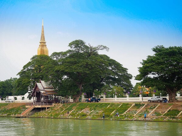 Un temple surmonté d’une flèche dorée, un pavillon et une étendue d’eau, avec des personnes et des véhicules à proximité.