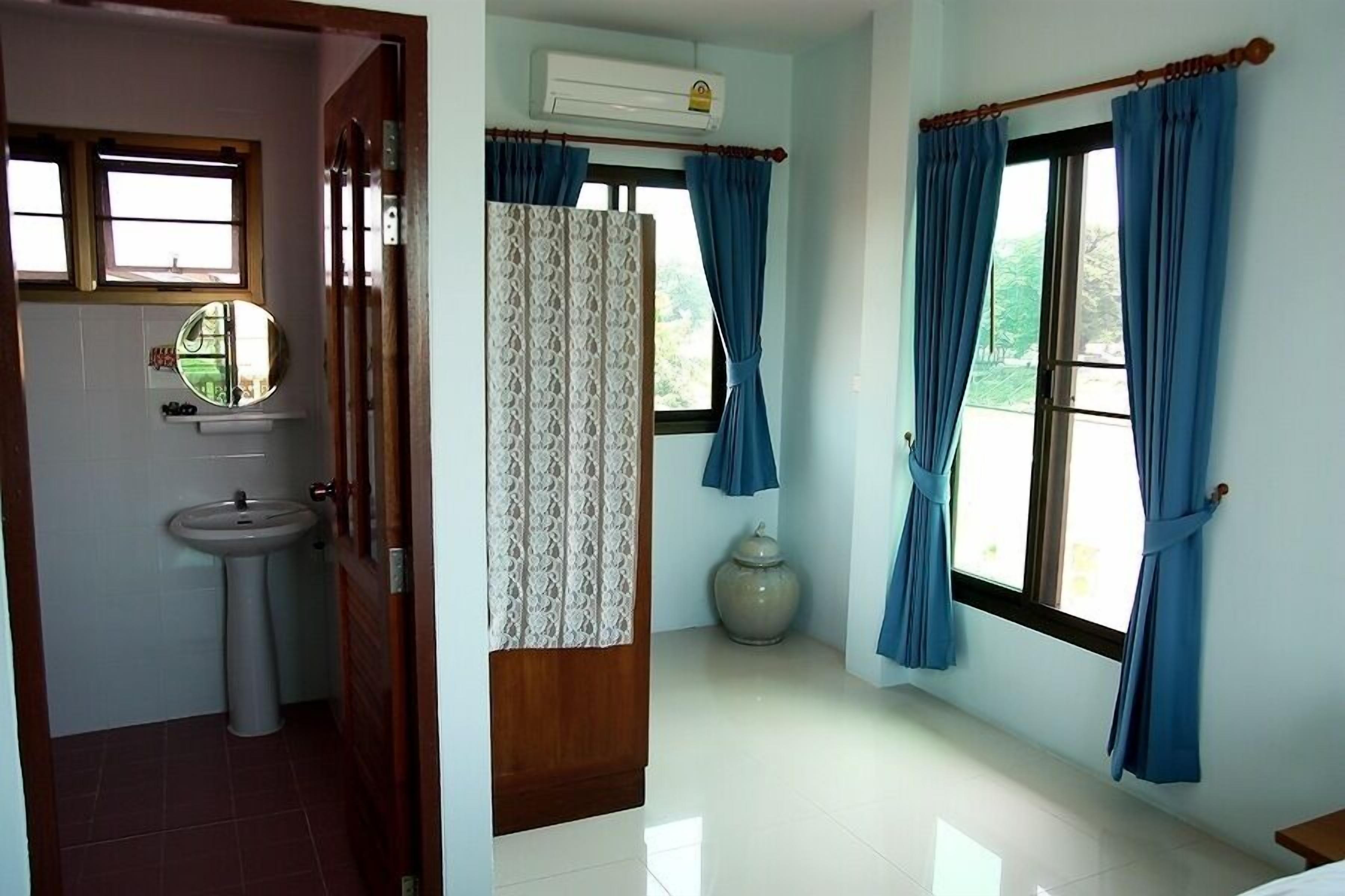 A room with a sink, mirror, and window with curtains.