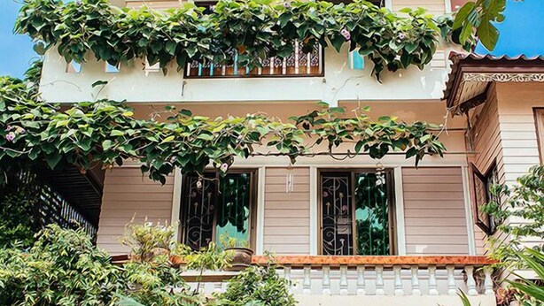 Un bâtiment à deux étages doté d’un balcon, entouré d’une végétation luxuriante et agrémenté de plantes en pot.