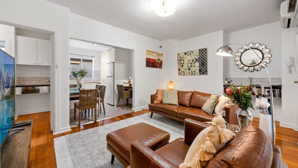 A modern living room with a brown leather sofa, a coffee table, and a dining area in the background.