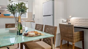 A modern kitchen with a glass dining table, wicker chairs, a white refrigerator, and a vase with greenery.