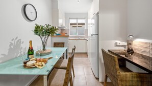 A modern kitchen with a dining area, featuring a glass table with food, a clock, and a plant.