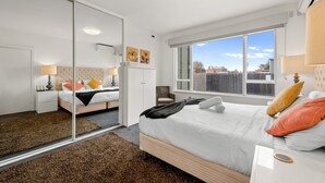 A modern bedroom with a large bed, a mirror, and a window with a view of the outside.