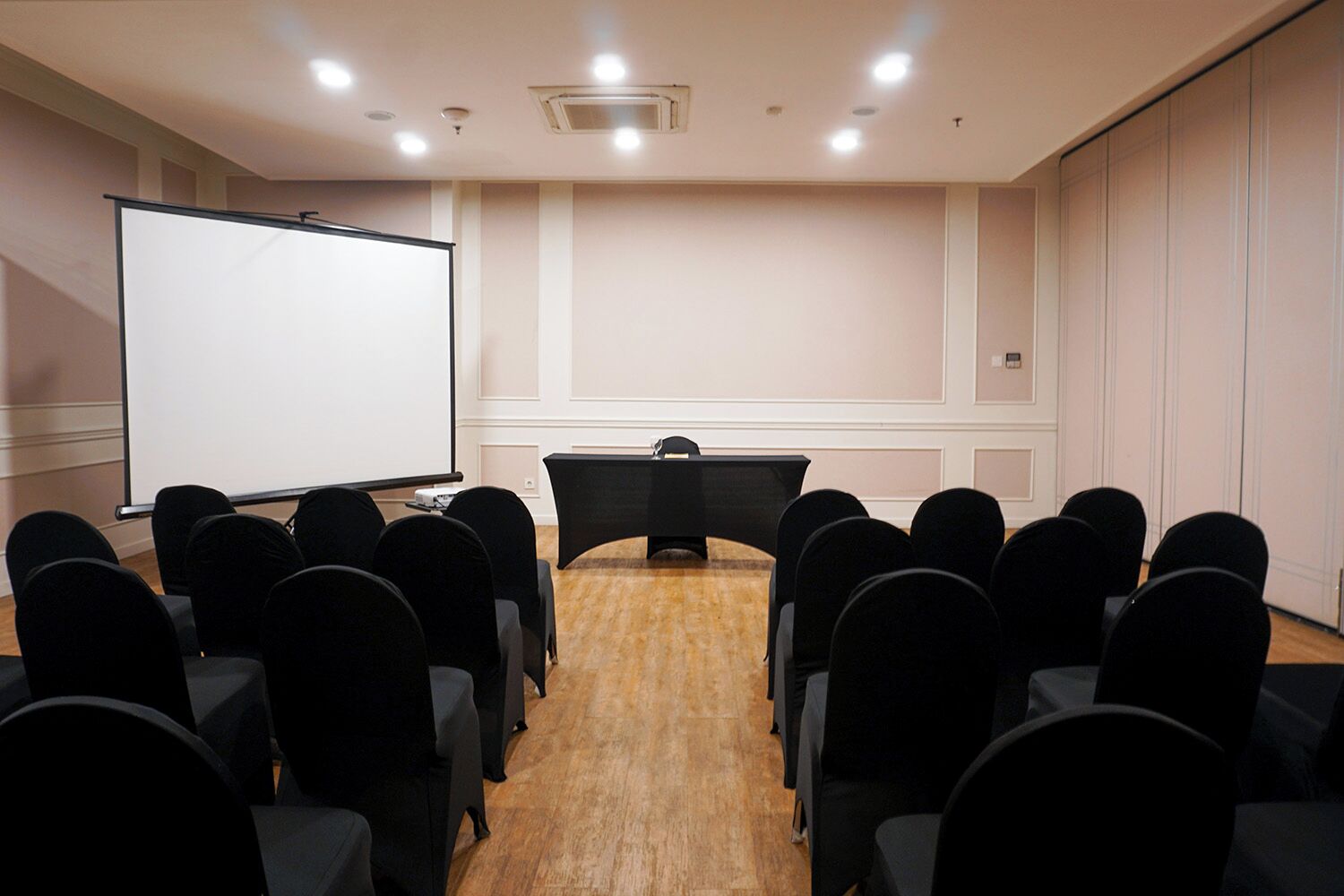 A conference room with a whiteboard, a projection screen, a table, and rows of chairs.