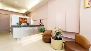 A reception area with a reception desk labeled "RECEPTION," two brown leather chairs, and a potted plant. - Tara Monte Hotel Pratunam (Bangkok)