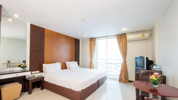 A hotel room with a bed, a desk, a chair, a TV, and an air conditioning unit. - Tara Monte Hotel Pratunam (Bangkok)