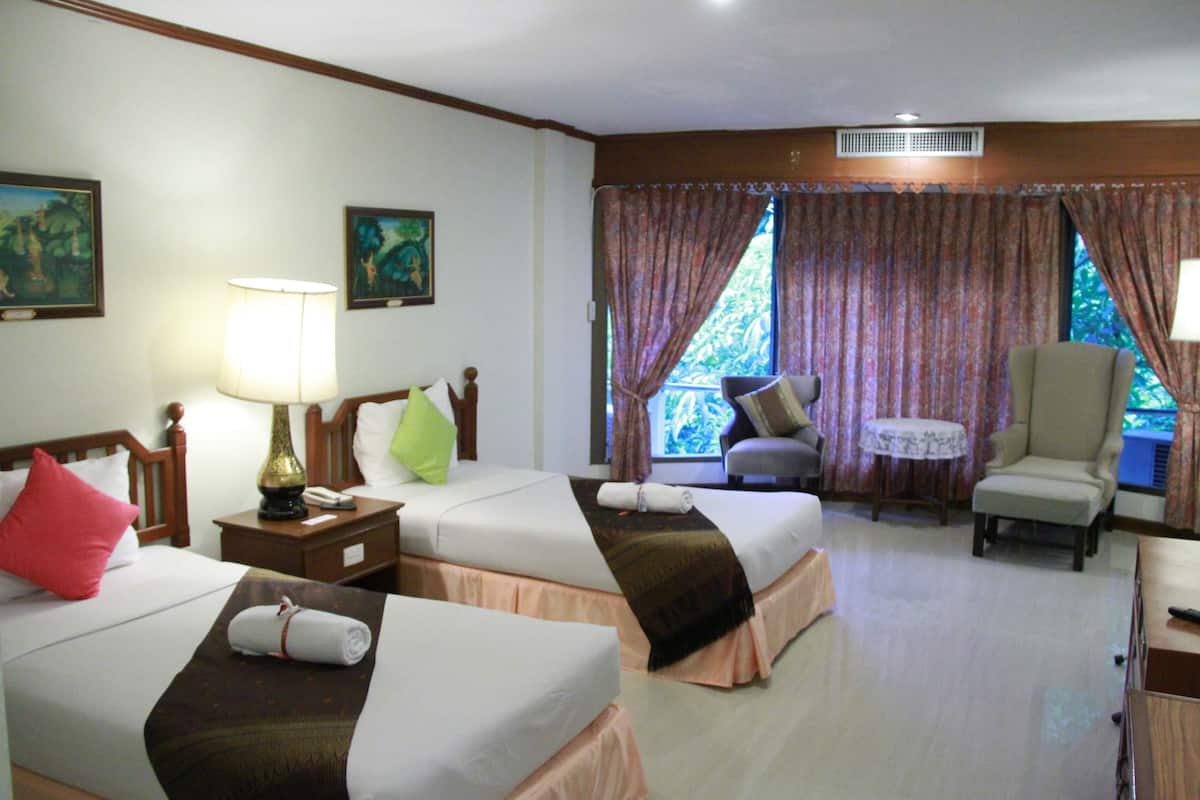 A hotel room with two beds, a chair, a table, and a window with curtains.
