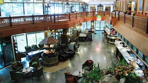 A spacious lobby with a high ceiling, a central seating area with sofas and chairs, a long reception desk, and a decorative railing overlooking the lobby.