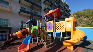 Un parque infantil con toboganes y estructuras para escalar, rodeado por un edificio con balcones.