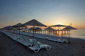 A beach with rows of sun loungers and thatched umbrellas.