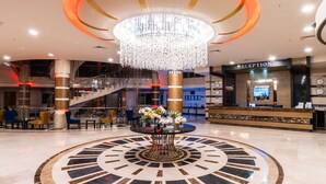 A lobby with a large circular floor design, a reception desk, and a chandelier. - Grand Ring Hotel (Kemer)