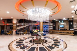 A lobby with a large circular floor design, a reception desk, and a chandelier. - Grand Ring Hotel (Kemer)