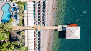 An aerial view of a resort with a swimming pool, beach area, and a large covered structure. - Grand Ring Hotel (Kemer)