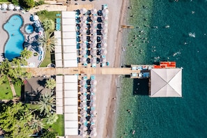 An aerial view of a resort with a swimming pool, beach area, and a large covered structure. - Grand Ring Hotel (Kemer)