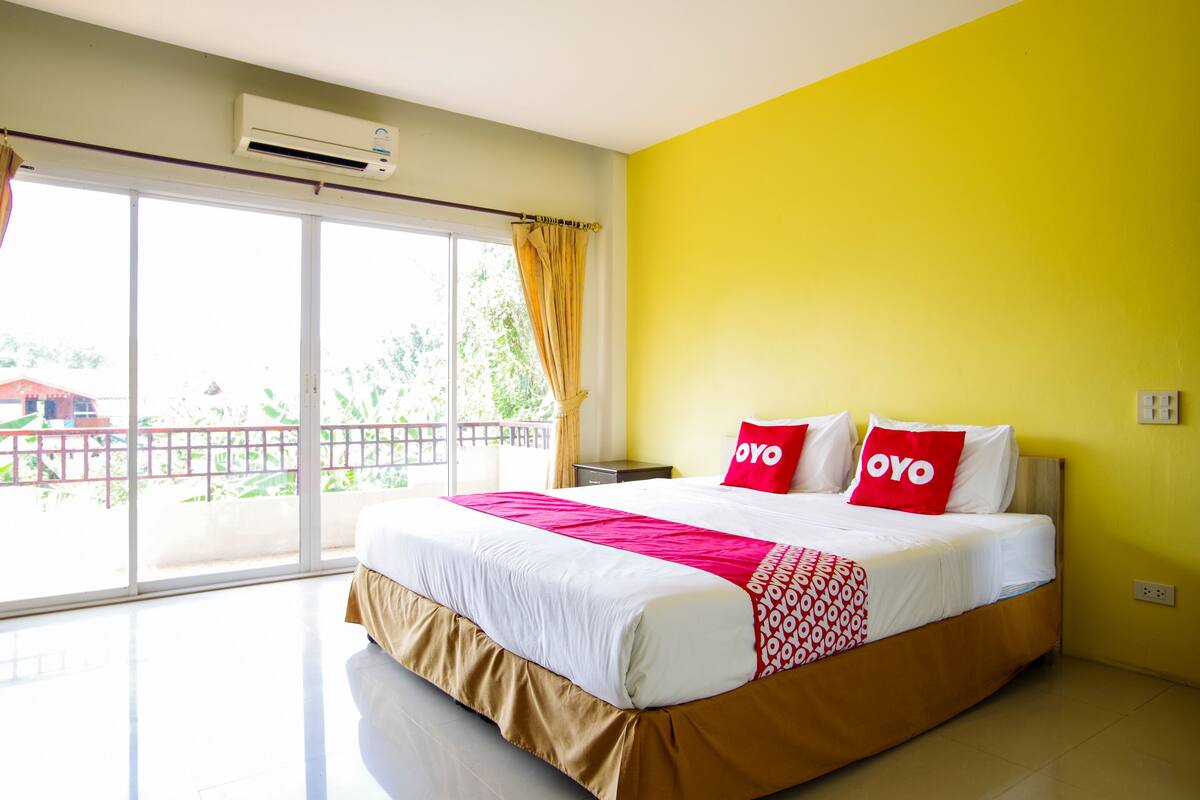 A hotel room with a large bed, yellow walls, and a balcony with a view.