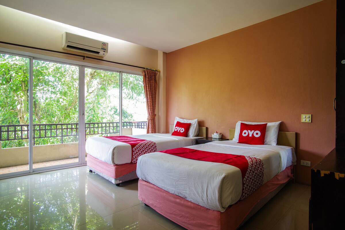 A hotel room with two beds, large windows, and a balcony.
