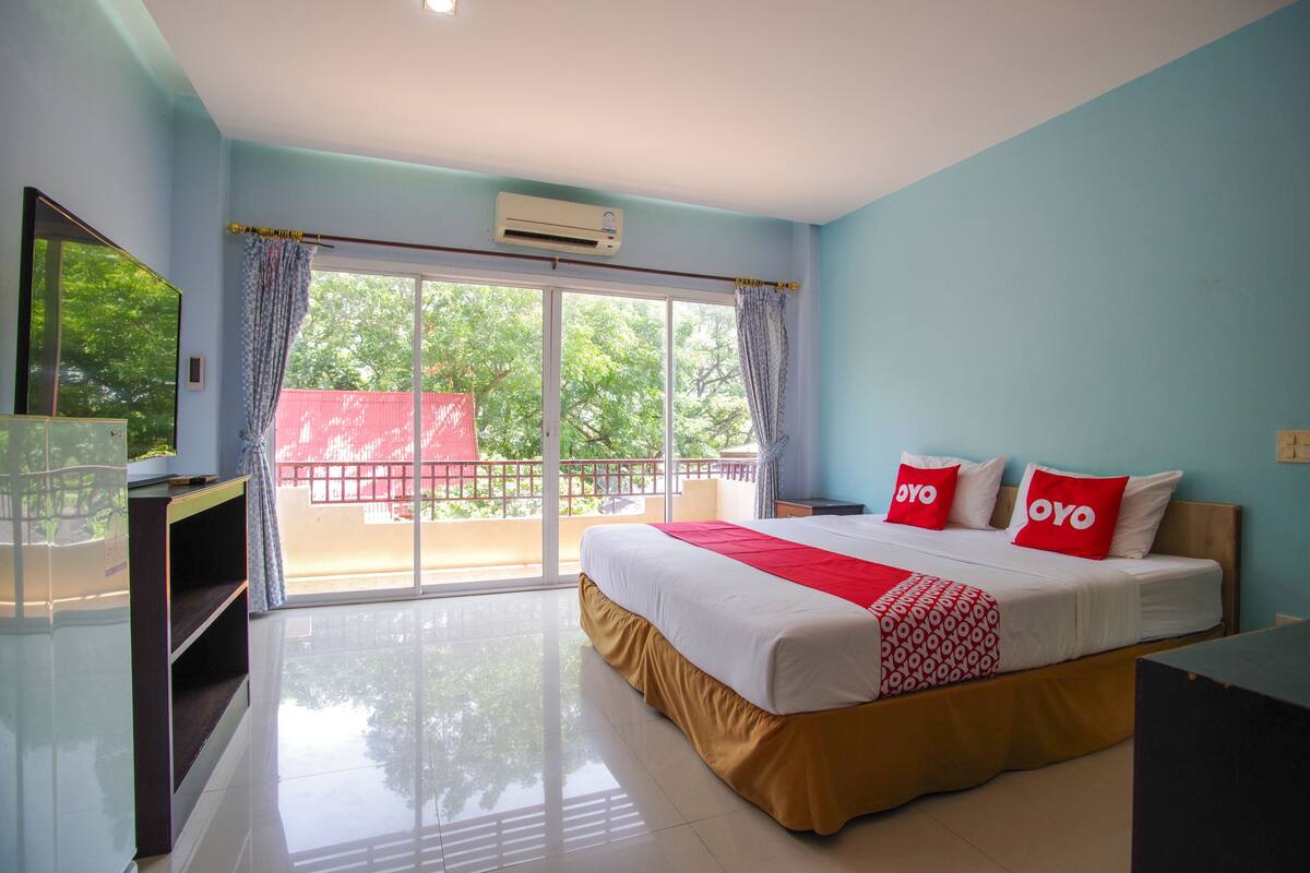 A hotel room with a large bed, a TV, and a balcony with a red fence.
