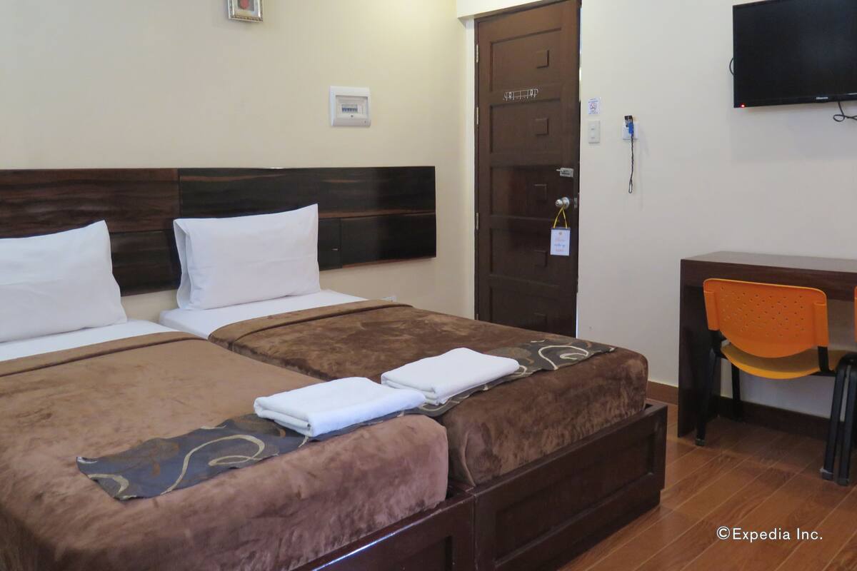Une chambre d’hôtel avec deux lits, un bureau, une chaise orange, une télévision et une porte.