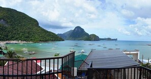A coastal view with boats, a mountain, and a building with a sloped roof. - Rovic's Tourist Hotel (El Nido)