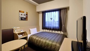 A hotel room with a bed, a desk, a chair, a television, and a window with curtains.