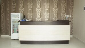 A reception desk with a patterned wallpaper background, a refrigerator with beverages, and a small shelf with items.