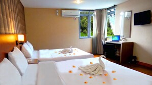A hotel room with two beds, a desk with a laptop, a TV, and a window with curtains.