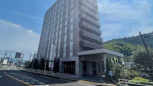 Un hotel de varios pisos con un diseño moderno, que cuenta con una entrada destacada y un cartel de estacionamiento que indica disponibilidad de carga para vehículos eléctricos.