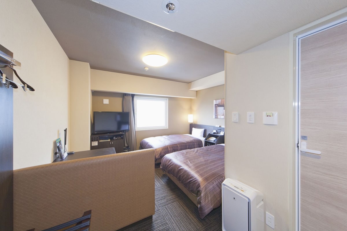 Une chambre d’hôtel avec deux lits, un bureau, une télévision et un réfrigérateur.