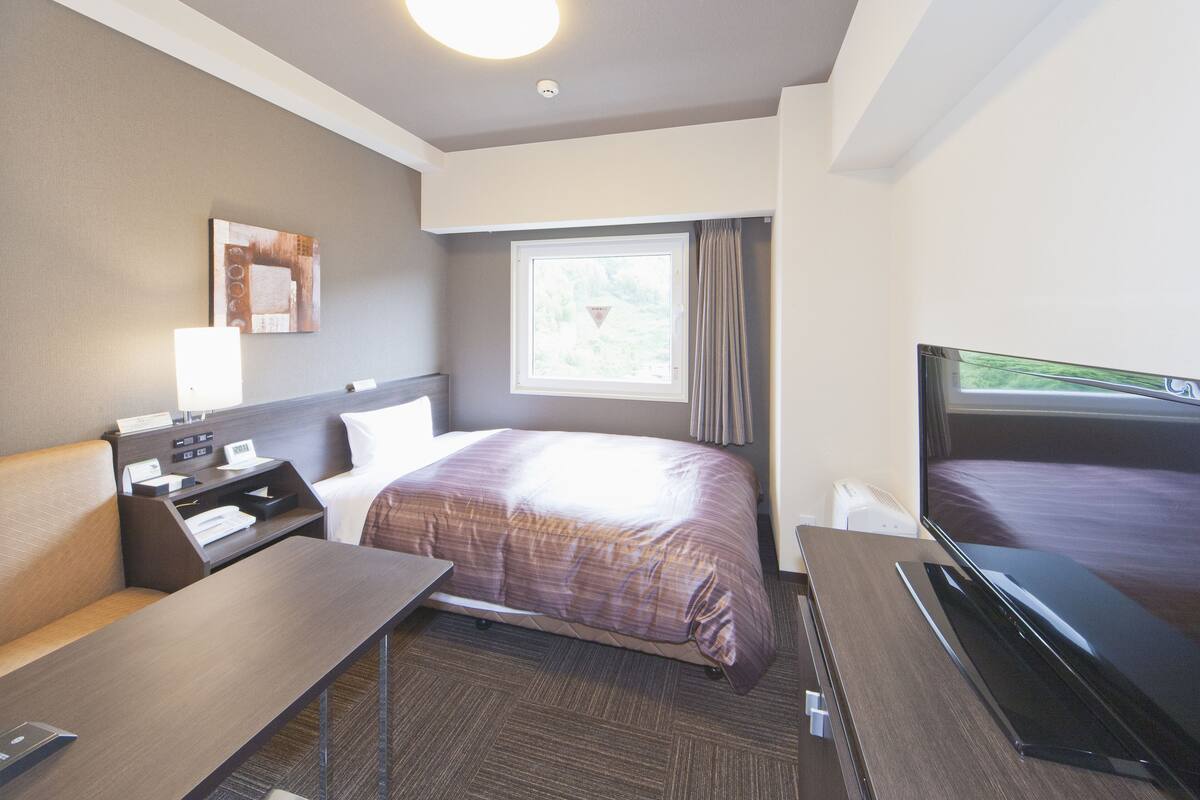 Une chambre d’hôtel équipée d’un lit, d’un bureau, d’une télévision, d’une fenêtre avec des rideaux et d’une œuvre d’art accrochée au mur.
