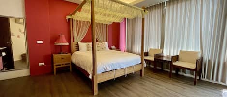 Una cama con dosel sobre cuatro columnas, con estructura de madera y colcha blanca, flanqueada por dos mesitas de noche con lámparas, un espejo y una silla.