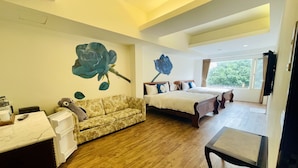 Habitación de hotel con piso de madera, un sofá, una cama con estructura de madera, un ventanal grande y un mural en la pared.