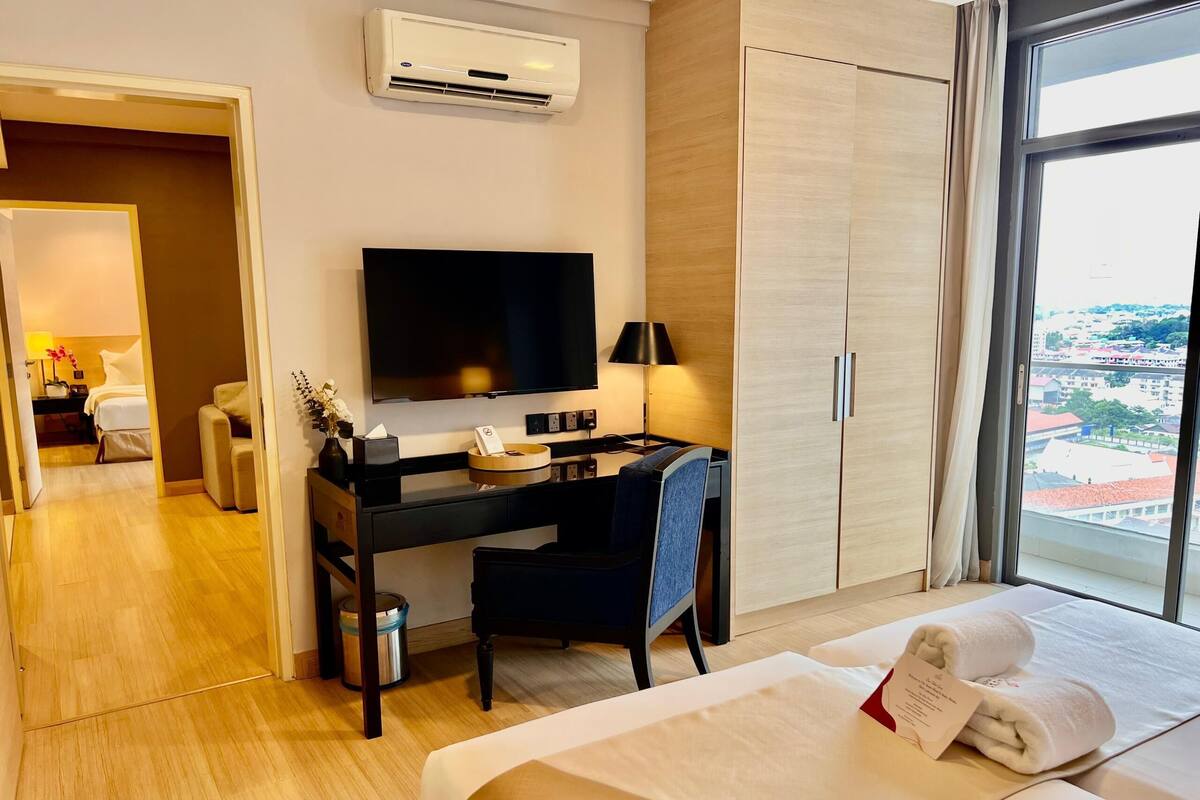 Habitación de hotel con cama, escritorio, televisión y vista a la ciudad.