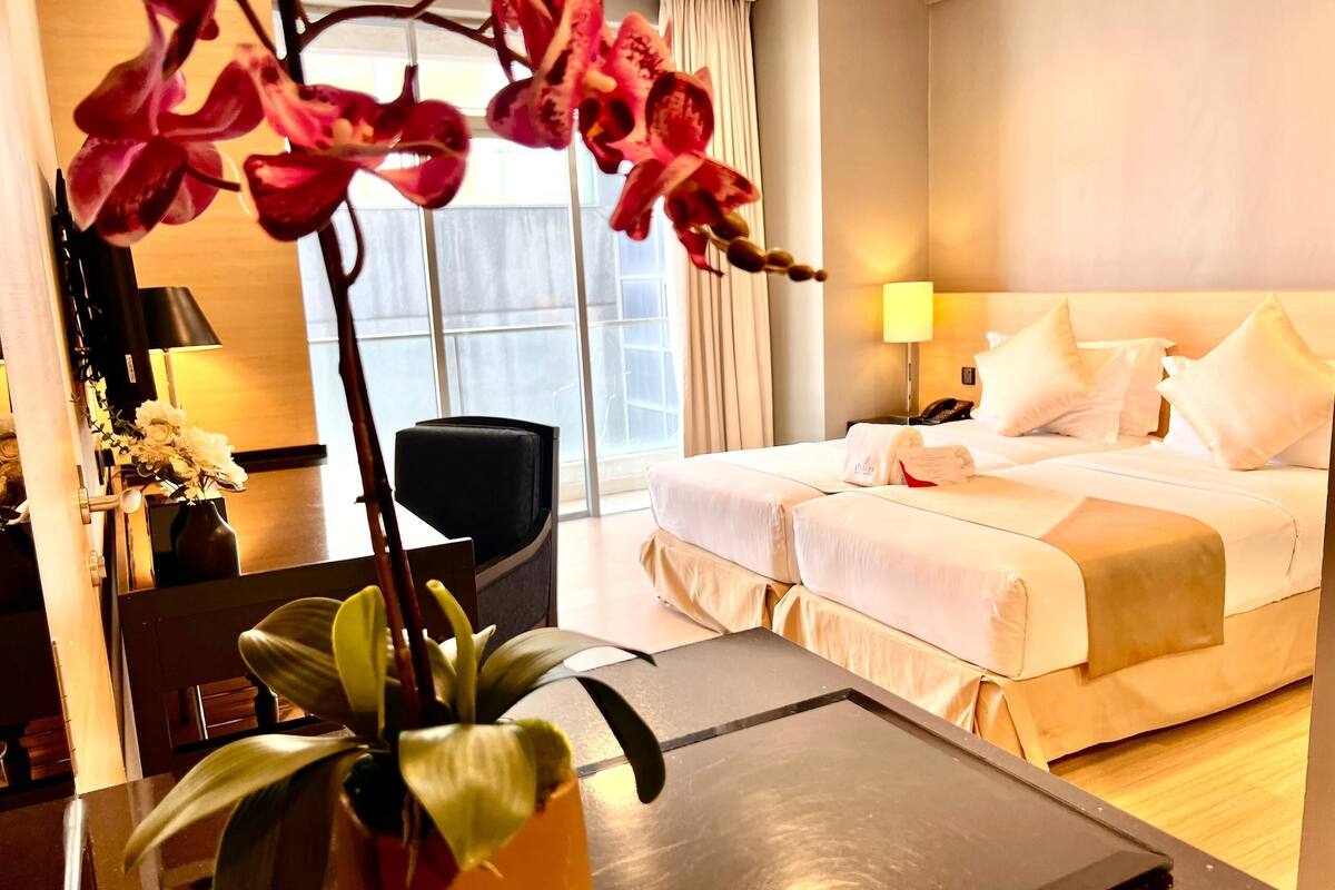 Una habitación de hotel con una cama, mesita de noche, lámpara y una planta en maceta.