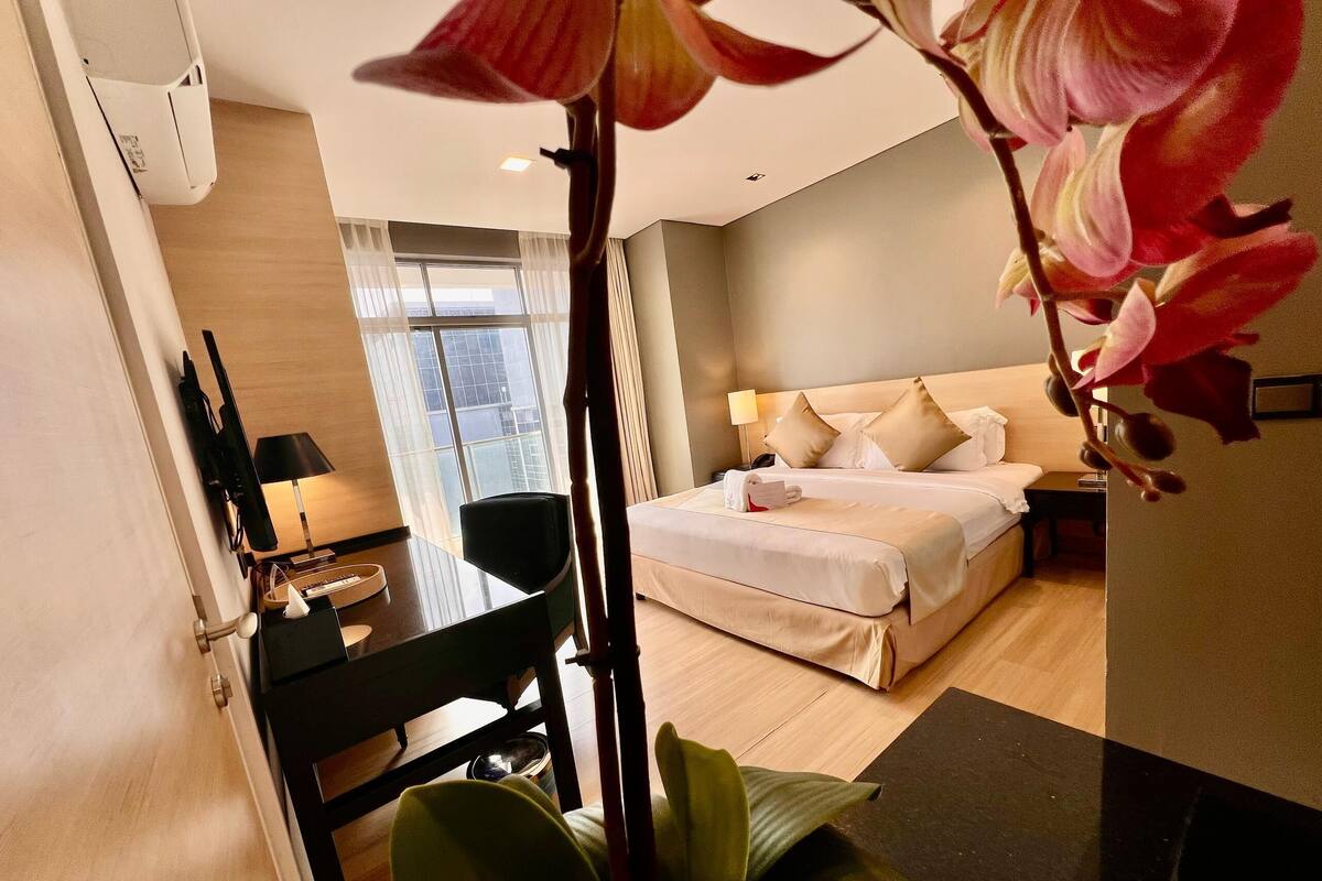 Habitación de hotel con cama, mesita de noche, lámpara y vistas a la ciudad desde la ventana.