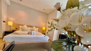 Ein Hotelzimmer mit einem ordentlich bezogenen Bett, einem Nachttisch mit Lampe und einer Vase mit Blumen.