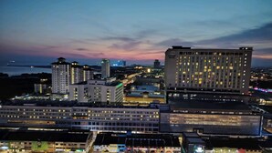 Ein Stadtbild im Dämmerlicht mit beleuchteten Gebäuden, darunter ein Hotel mit mehreren Etagen und einer auffälligen Beschilderung.