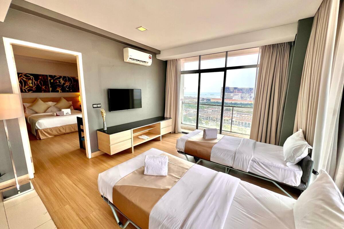 Habitación de hotel con dos camas, televisión, escritorio y ventana grande con vista a la ciudad.